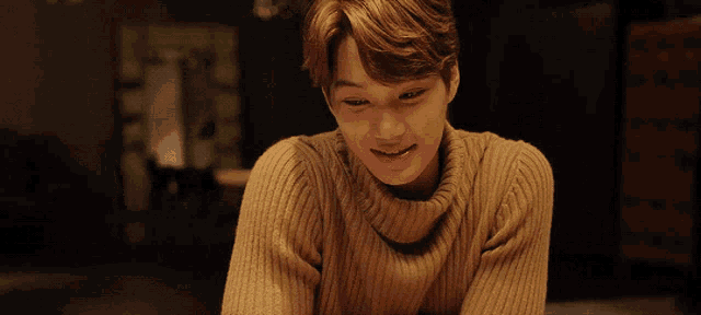a young man wearing a turtleneck sweater is sitting at a table