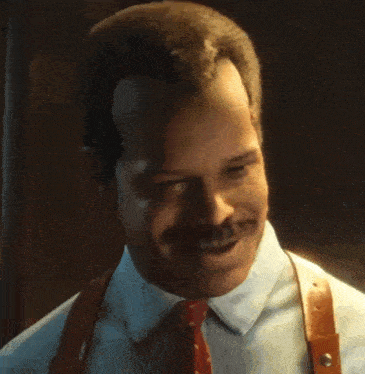 a man with a mustache is wearing suspenders and smiling