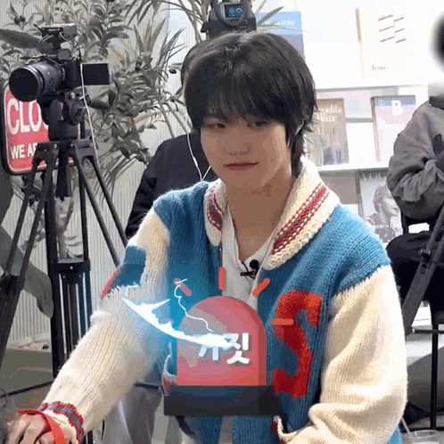a man in a blue and white sweater is standing in front of a camera and a sign that says clo