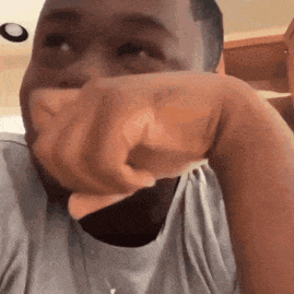 a man is covering his mouth with his hand while pointing at the camera .