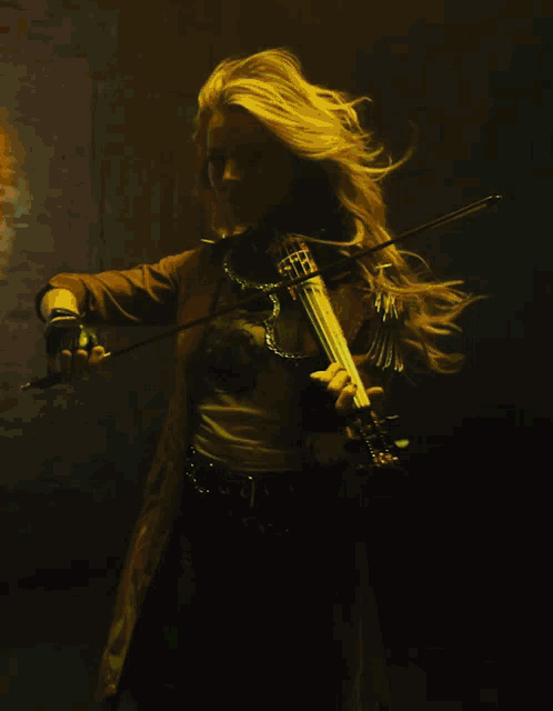 a woman with long blonde hair is playing a violin in a dark room