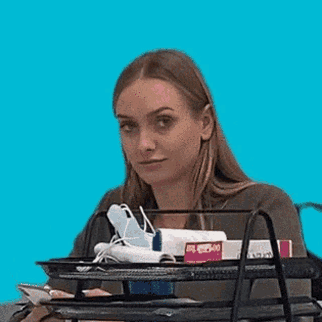 a woman is sitting at a desk making a funny face while holding a book .