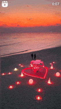 a couple is standing on a beach with a heart shaped table and candles .
