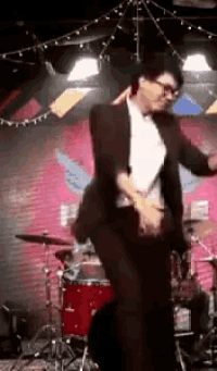 a man in a suit is dancing on a stage with a drum set in the background