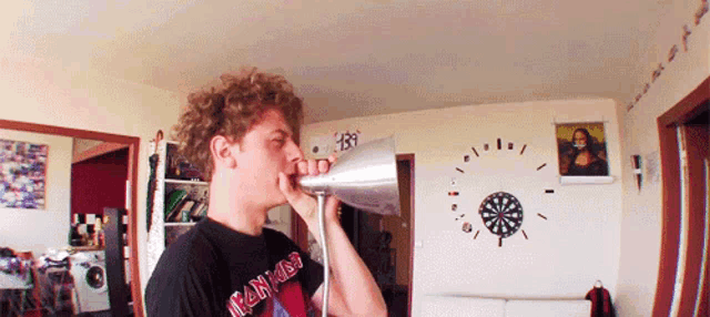 a man wearing an iron maiden shirt holds a megaphone in front of a dart board