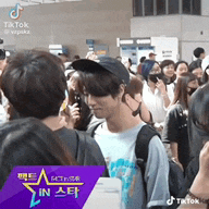 a man wearing a hat is standing in a crowd of people in front of a sign that says tiktok .