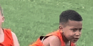 a boy in an orange shirt is sitting in the grass with a girl .
