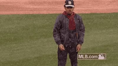 a man is standing on a baseball field wearing a jacket and hat .