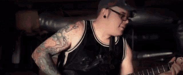 a man with a lot of tattoos on his arms is holding a microphone in a dark room .
