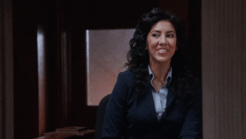 a woman in a suit sits in a dark room smiling