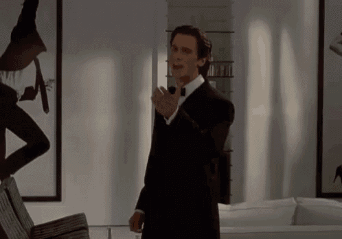 a man in a tuxedo and bow tie is standing in a living room holding a microphone .