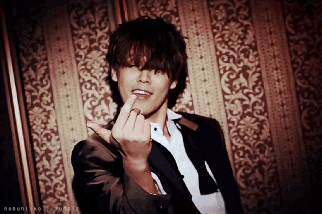 a man in a suit is giving the middle finger in front of a patterned wall