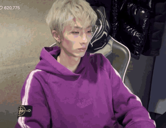 a man wearing a purple stone island hoodie sits on a chair