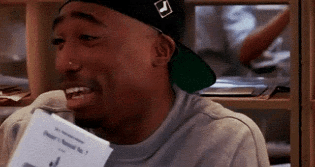 a man wearing a hat and holding a piece of paper with the word ' tupac ' on it .