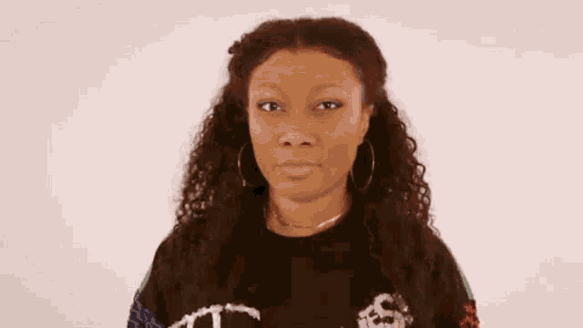 a woman with curly hair and hoop earrings is wearing a black shirt and making a funny face .