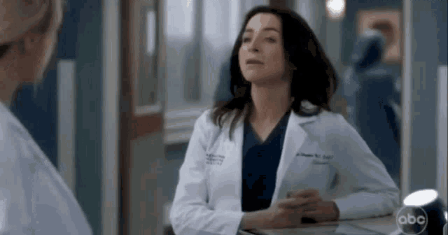 a woman in a white lab coat is sitting at a table in a hospital .