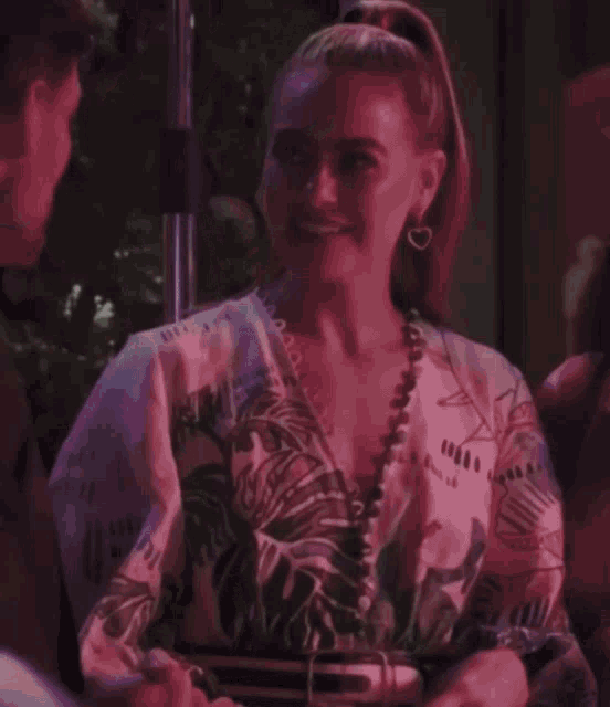 a woman with a ponytail is smiling and wearing a floral shirt