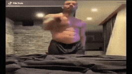 a man without a shirt is standing on a bed and pointing at something