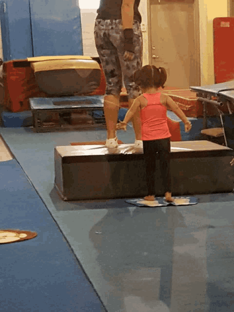 a little girl in a pink tank top is standing on a bench