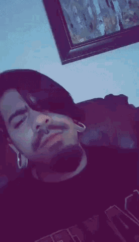 a man with a beard and ear plugs is laying on a couch with his eyes closed