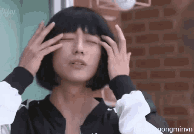 a woman with short black hair is holding her hands to her head .