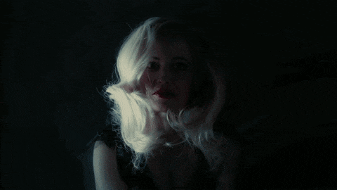 a woman with blonde hair and red lips is smiling in a dark room