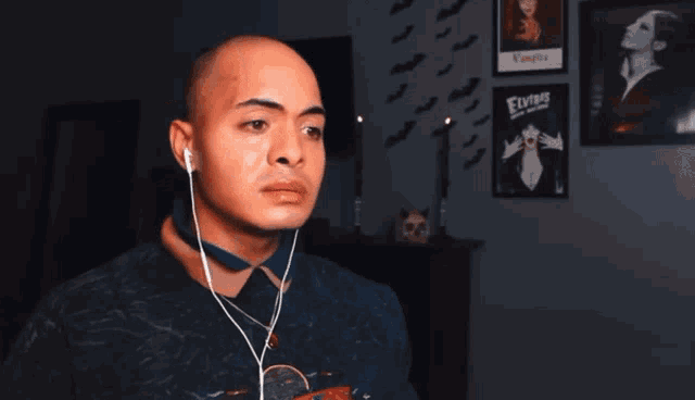 a bald man wearing ear buds stands in front of a vampire poster on the wall