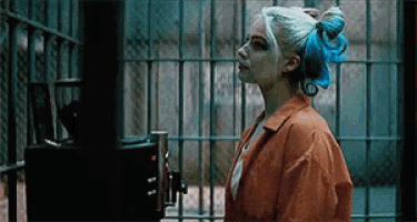 harley quinn is standing in a prison cell with a blue ribbon in her hair .