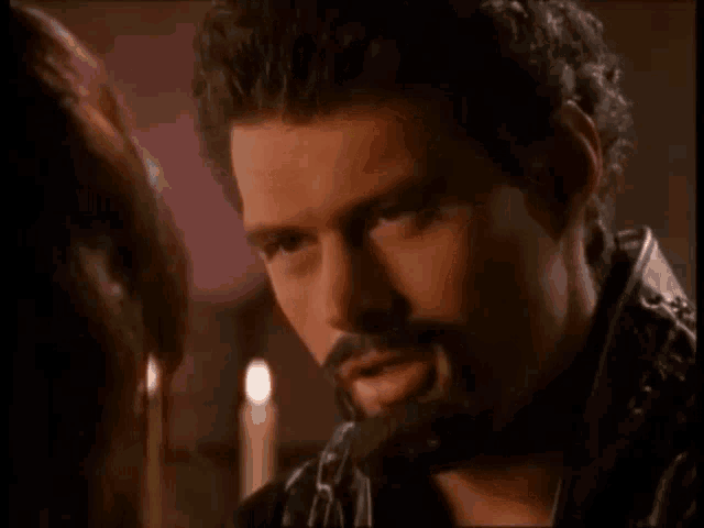 a man with a beard is talking to a woman with the words now tell me above him