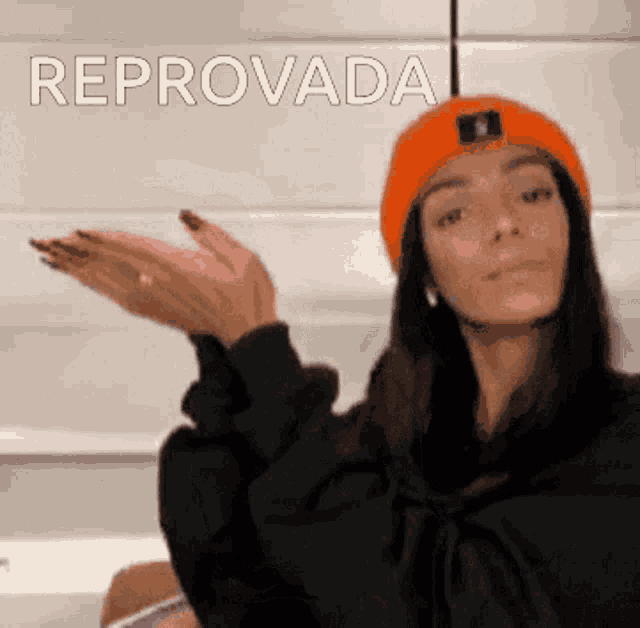 a woman wearing an orange hat and a black hoodie is making a gesture with her hands and the word reprovada is behind her
