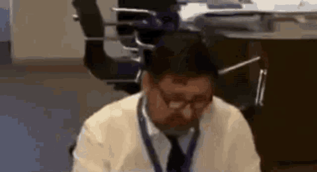 a man wearing glasses and a lanyard is sitting at a desk in a room .