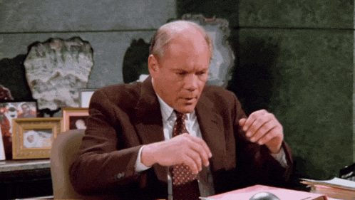 a man in a suit and tie is sitting at a desk looking at papers