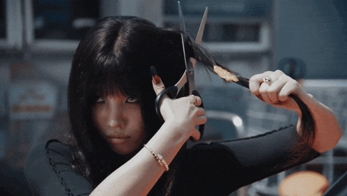 a woman is cutting her hair with scissors while wearing a bracelet