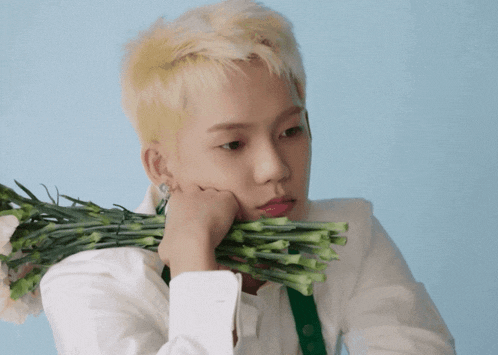 a young man with blonde hair is holding a bunch of green flowers in his hand