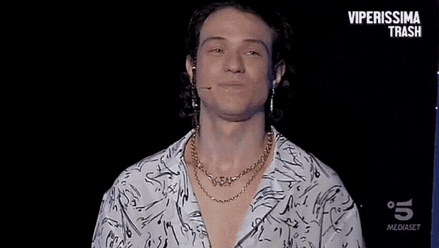 a young man wearing a necklace and earrings stands in front of a sign that says " viperissima trash "