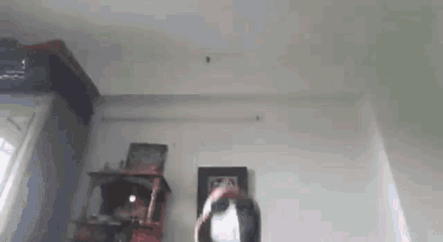 a person is standing in a room with a picture on the wall and looking up at the ceiling .