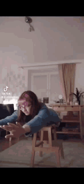a girl wearing glasses and a headband is laying on a stool with her arms outstretched