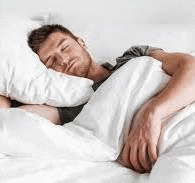 a man is sleeping in bed with white sheets and pillows .