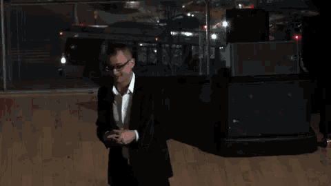 a man in a black suit and white shirt is giving the peace sign
