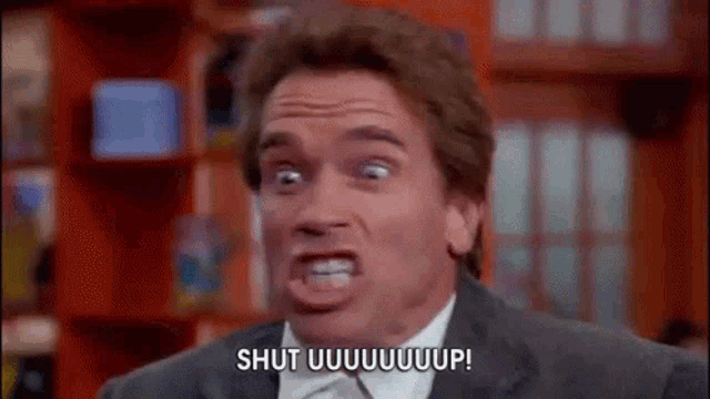 a man in a suit and tie is making a funny face and saying shut uuuuuuup .
