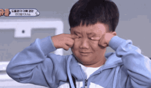 a young boy in a blue hoodie is crying and covering his eyes