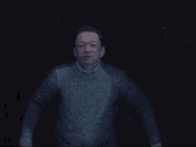 a man in a grey sweater stands in the dark