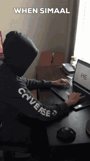 a person wearing a black converse sweatshirt is typing on a laptop