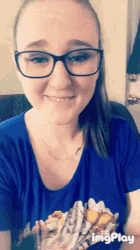 a woman wearing glasses and a blue shirt is smiling while holding a piece of paper that says imgplay