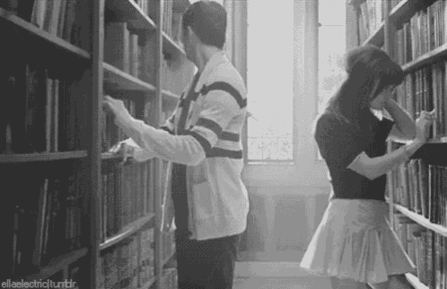 a man and a woman are in a library looking at books .