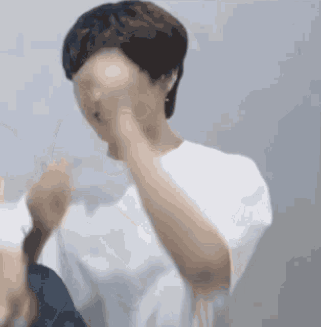 a man wearing a white shirt is covering his face with his hand .