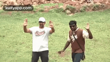 two men are standing in a grassy field with their hands up .