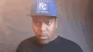 a man wearing a kc hat is making a funny face while smoking a cigarette .