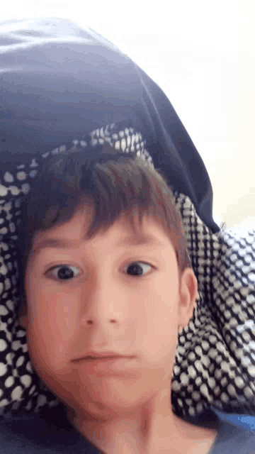 a young boy laying on a bed with a black and white blanket on his head