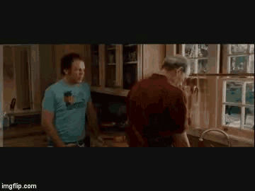 a man in a blue shirt is standing next to another man in a kitchen .